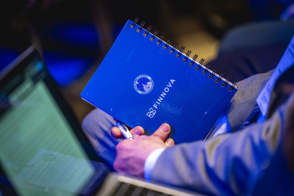 Cuaderno azul con los logos de la Dirección Nacional del Antártico y de FINNOVA, en manos de un participante de la reunión