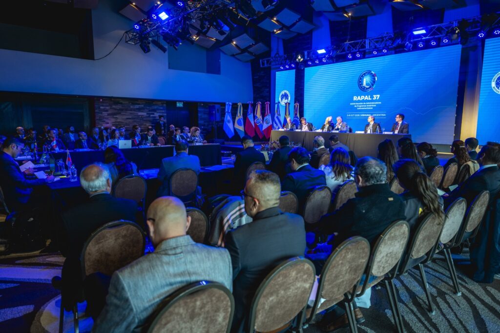 Vista de la Sala Plenaria con las delegaciones sentadas frente a la mesa de apertura, bajo la pantalla de la RAPAL 37
