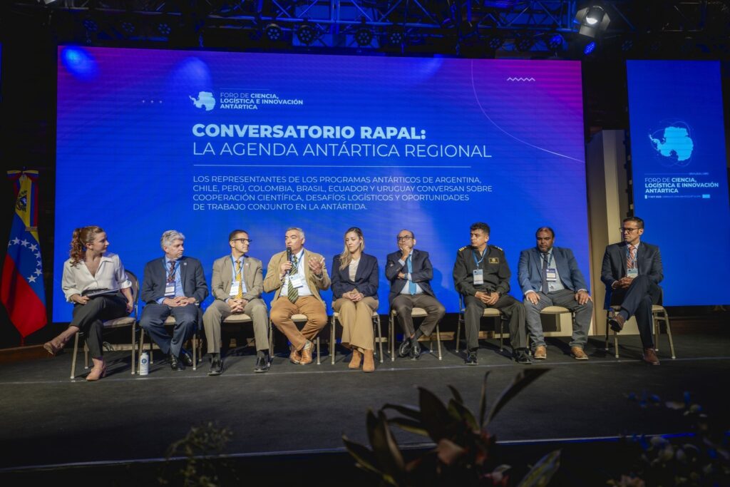 Panel de programas antárticos en el conversatorio RAPAL, con un expositor hablando frente a la pantalla y las banderas