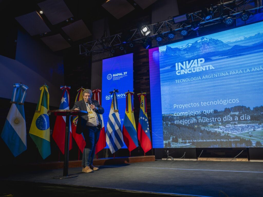 Expositor de INVAP en el atril, frente a las banderas de los países y la pantalla de la presentación