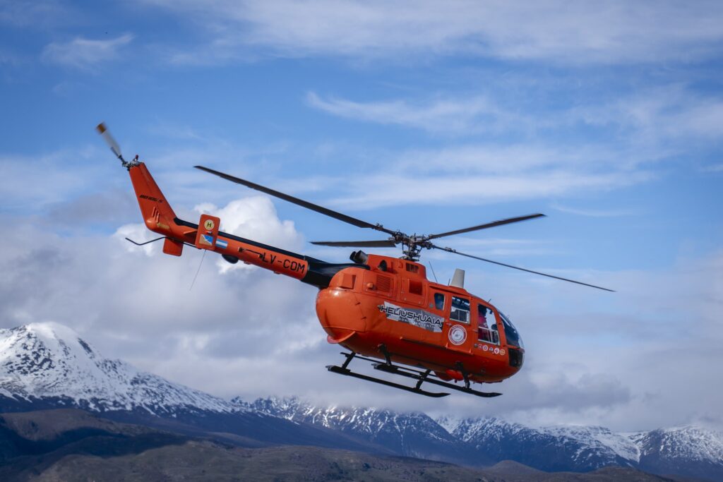 Helicóptero naranja de HeliUshuaia en vuelo contra la cordillera nevada