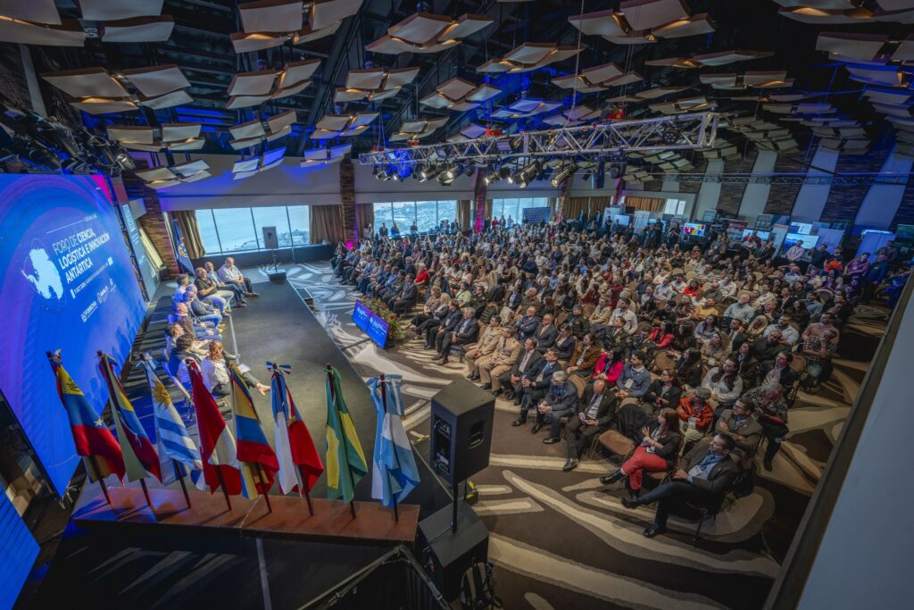 Salón lleno visto desde el escenario del Foro de Ciencia, Logística e Innovación Antártica, con banderas y la pantalla del evento
