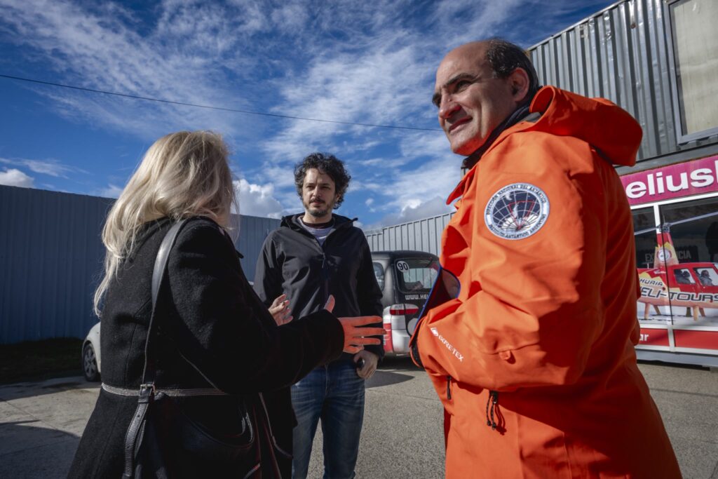 Una persona con campera naranja de la Dirección Nacional del Antártico conversa con otras dos frente al local de HeliUshuaia